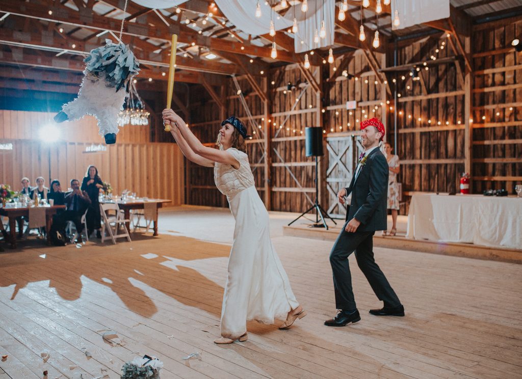 wedding day bride and groom hit piñata during reception in catskills barn 